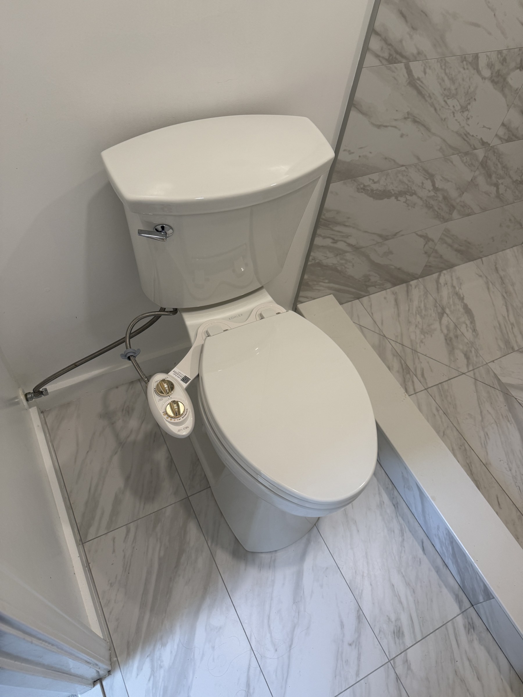 Bidet attachment installed on toilet in marble tile bathroom — clean professional install