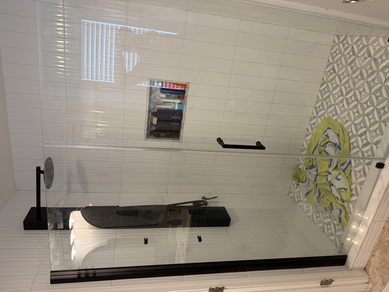 Frameless glass shower door installed with matte black hardware — clean modern finish against white subway tile and patterned accent wall