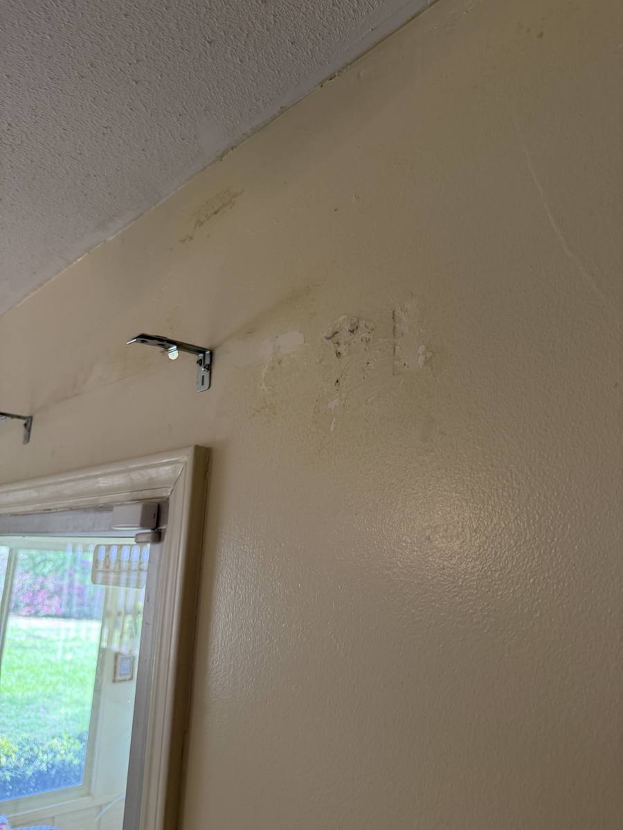 Water damaged drywall with peeling paint and old curtain rod hardware — before repair